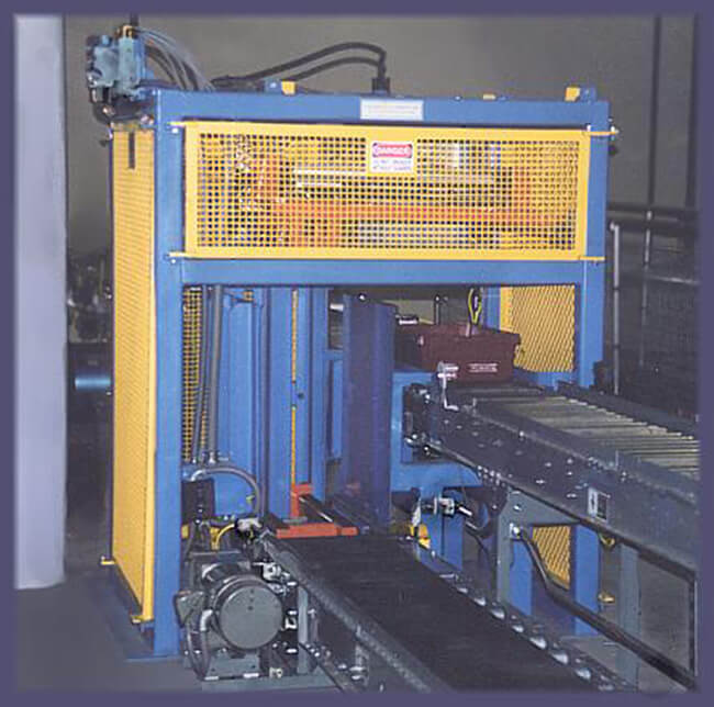 Tote Lidding Machine installed; with the lid stack delivery conveyor seen on the lower left; with the totes being delivered on the upper right.